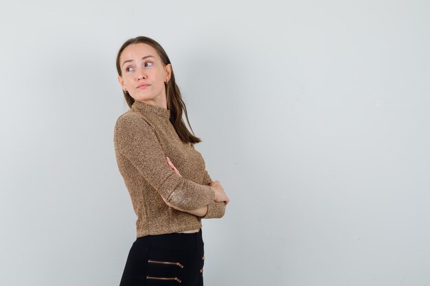 Young female looking back while keeping arms crossed in golden blouse and looking focused . space for text