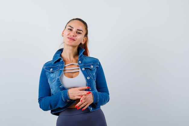 Young female looking at camera in crop top, jacket, pants and looking confident. front view.