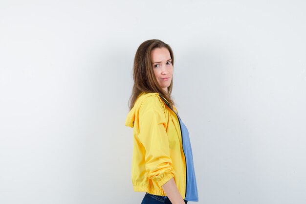 Young female looking at camera over her shoulder in t-shirt, jacket and looking delightful. .