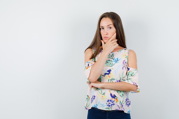 Young female looking at camera in shirt, jeans and looking pensive , front view.