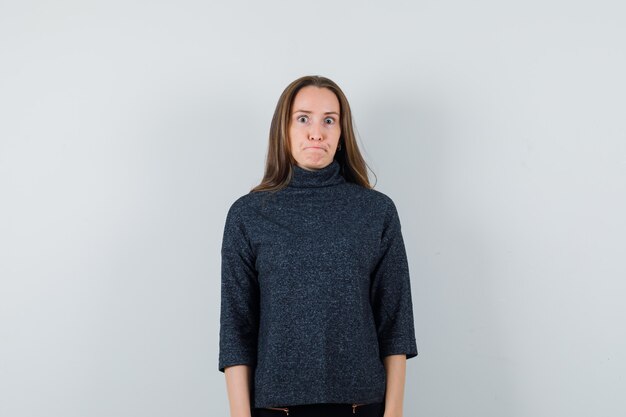 Young female looking at camera with widely opened eyes in black blouse and looking displeased 