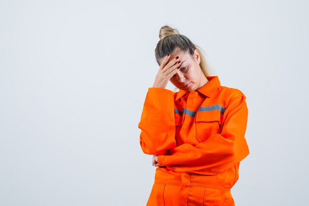 Giovane femmina guardando verso il basso tenendo la mano sulla testa in uniforme da lavoro e guardando sconvolto. vista frontale.