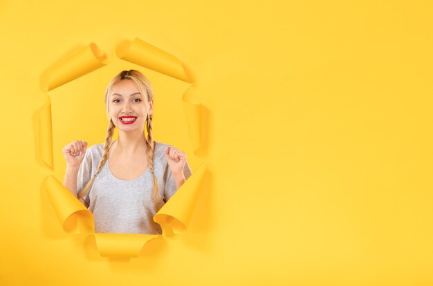 Young female looking from the torn yellow paper background sale indoor window facial