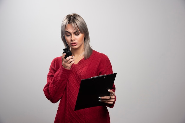 Young female looking at radio transceiver on gray background.