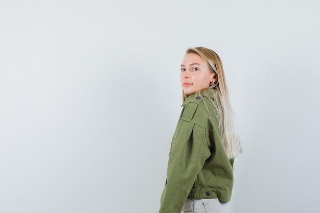 Молодая женщина смотрит через плечо в зеленой куртке, джинсах и выглядит разумно. . место для текста