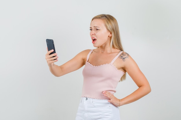 Young female looking at smartphone in singlet, mini skirt and looking sorry.