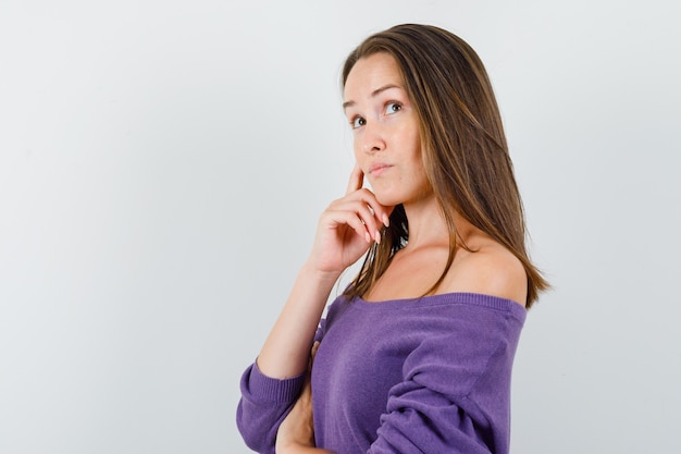 Young female looking up in violet shirt and looking thoughtful. .