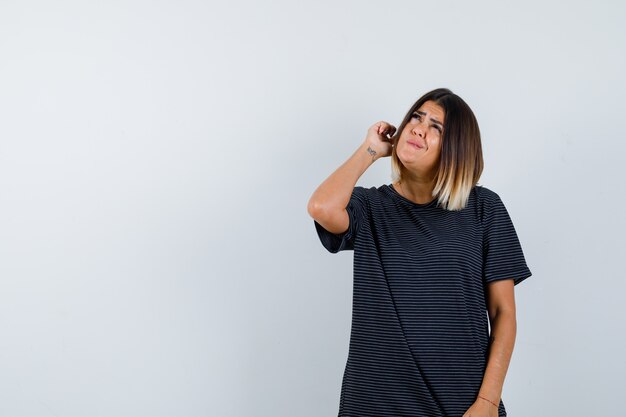 Young female looking up while thinking in polo dress and looking pensive , front view.