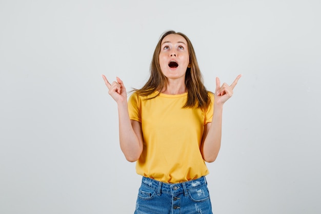 Giovane donna che osserva in su con il gesto della pistola in t-shirt, pantaloncini vista frontale.