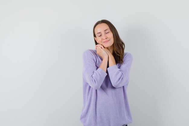 Young female making pillow gesture in lilac blouse and looking sleepy. front view. free space for your text