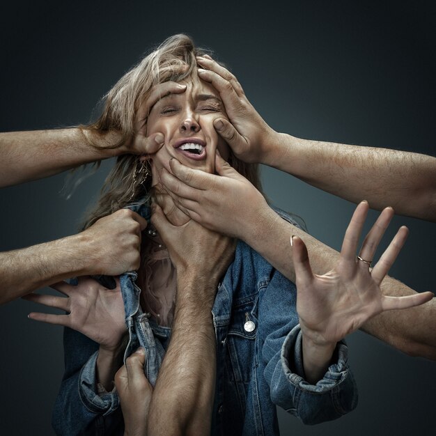 A young female model surrounded by male hands like her own thoughts or problems on dark wall