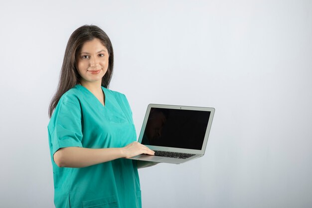 Young female nurse with laptop standing on white. 