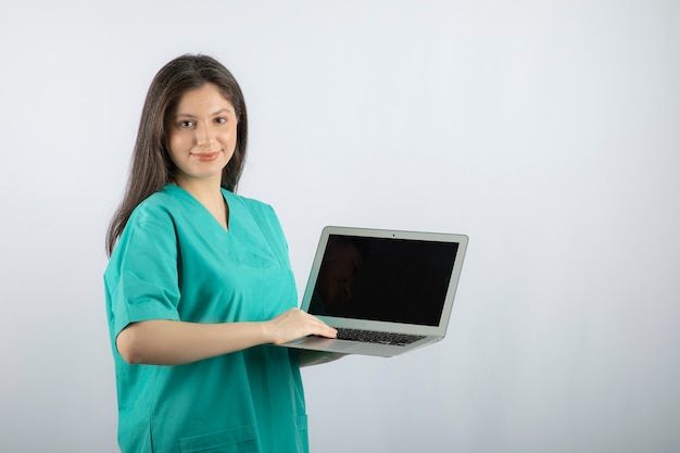 Young female nurse with laptop standing on white. 