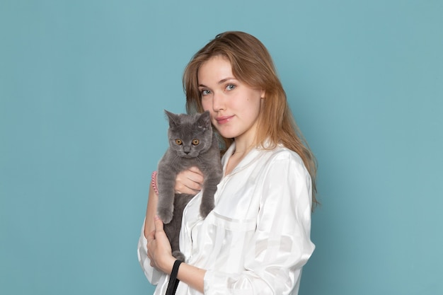 Free photo young female in pajamas and holding little cute grey kitten on blue