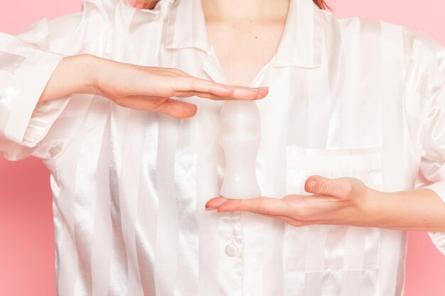 young female in pajamas and sleep mask holding make-up spray on pink