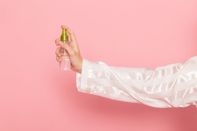 young female in pajamas and sleep mask holding make-up spray on pink