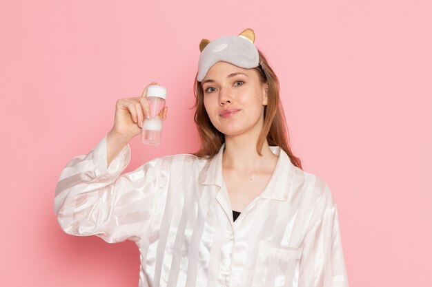 young female in pajamas and sleep mask holding spray can with smile on pink