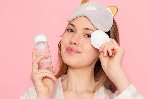 young female in pajamas and sleep mask holding spray on pink