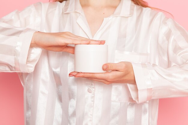 young female in pajamas and sleep mask holding white cream can on pink