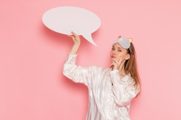 young female in pajamas and sleep mask holding white sign on pink