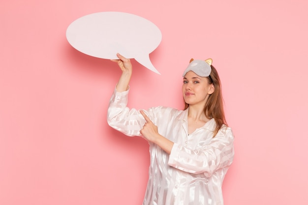 young female in pajamas and sleep mask holding white sign on pink