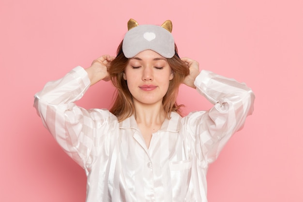 young female in pajamas and sleep mask posing smiling on pink