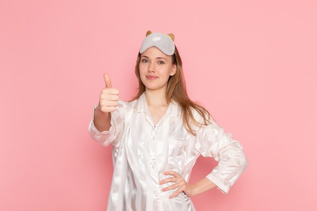 young female in pajamas and sleep mask posing and smiling on pink