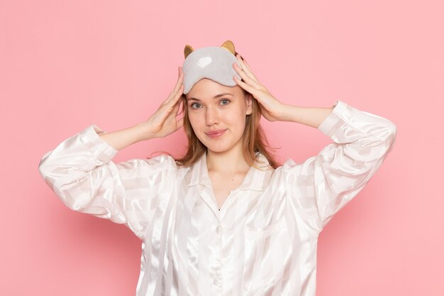 young female in pajamas and sleep mask posing with smile on her face on pink