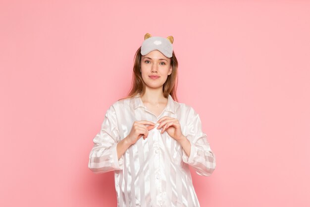 young female in pajamas and sleep mask posing with smile on pink