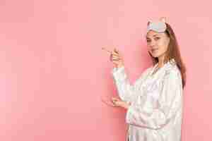 Free photo young female in pajamas and sleep mask posing with smile on pink