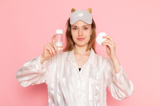 young female in pajamas and sleep mask smiling and holding sprays on pink