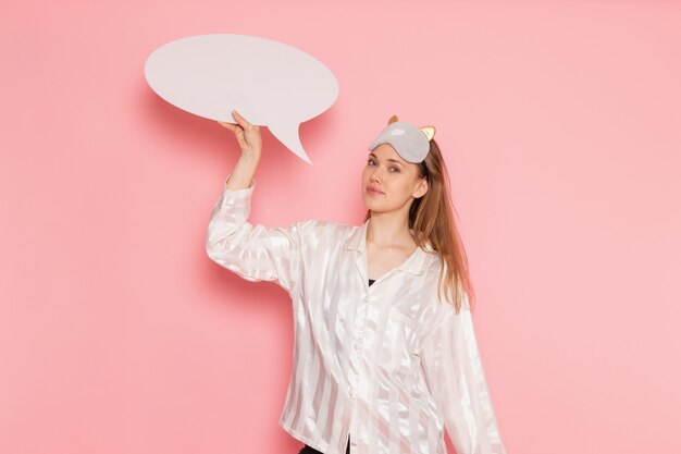 young female in pajamas and sleep mask smiling and holding whit sign on pink