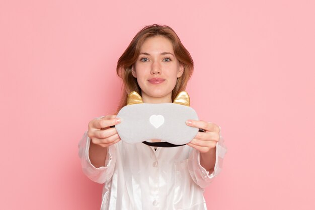 young female in pajamas and sleep mask smiling on pink