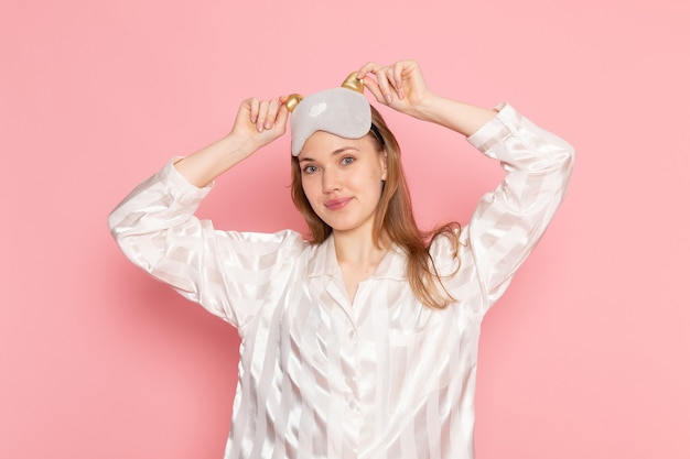 young female in pajamas and sleep mask smiling and posing on pink