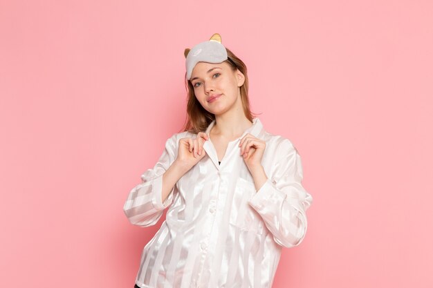 young female in pajamas and sleep mask standing and posing with smile on pink