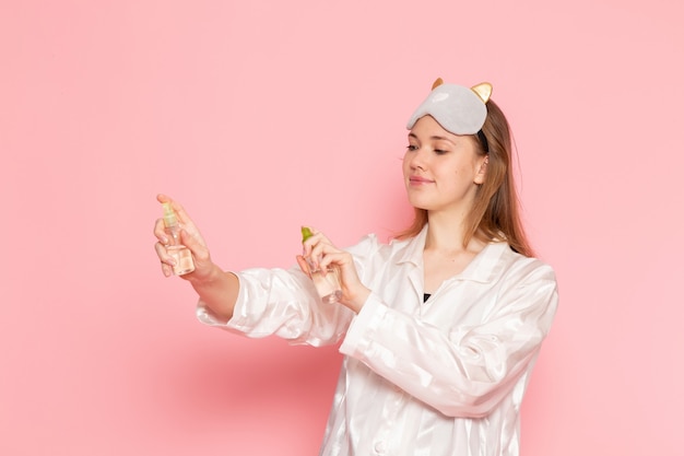 young female in pajamas and sleep mask using body spray on pink