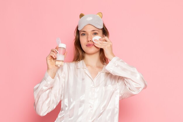 young female in pajamas and sleep mask using make-up spray on pink