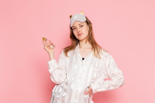 パジャマとスリープマスクのメイクアップスプレーを使用して、ピンクのポーズで若い女性