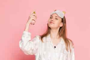 Free photo young female in pajamas and sleep mask using spray on pink