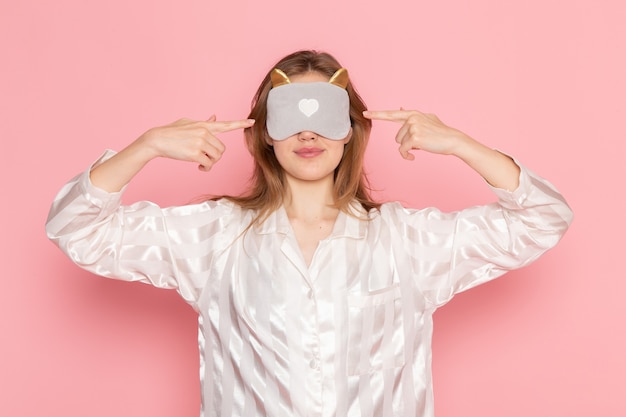 Free photo young female in pajamas and sleep mask with closed eyes on pink