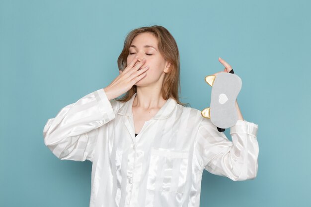 young female in pajamas and sleep mask yawning on blue