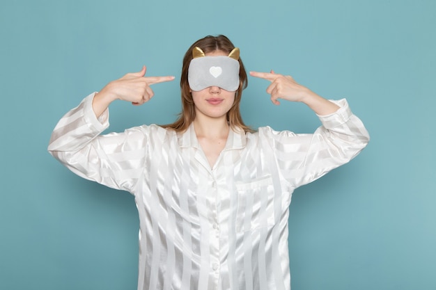 young female in pajamas wearing sleep mask on blue