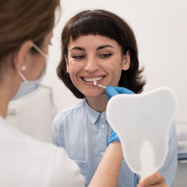 Young female patient looking in the mirror to check teeth matching before dental procedure