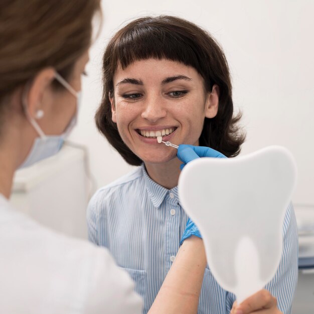 鏡を見て、歯科処置の前に歯のマッチングをチェックする若い女性患者