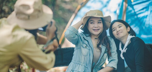 Young female photographer enjoy to take photo her friends she use digital camera and lovely girl pose at camping tent in nature forest copy space