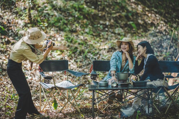若い女性写真家は、彼女がデジタルカメラを使用している彼女の友人と自然の森のコピースペースのキャンプテントでポーズをとる素敵な女の子の写真を撮ることを楽しんでいます