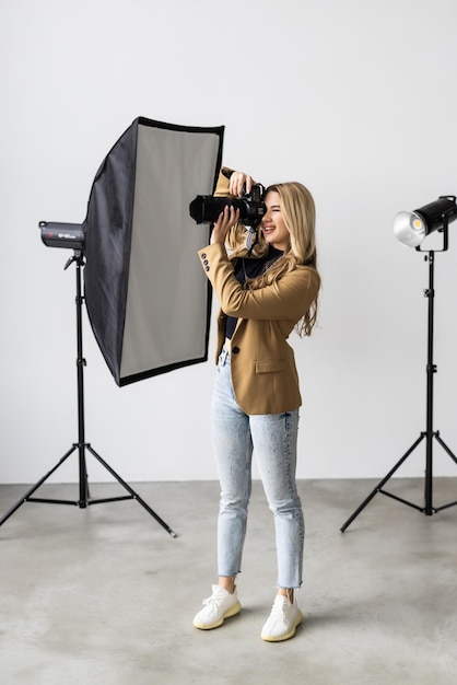 Young female photographer posing in the photo studio smiling and holding a professional digital camera