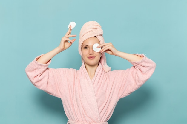 Foto gratuita giovane donna in accappatoio rosa dopo la doccia che pulisce il suo trucco sul blu