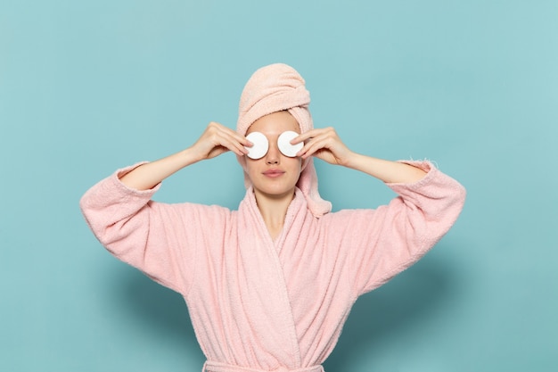 Free photo young female in pink bathrobe after shower covering her eyes on blue