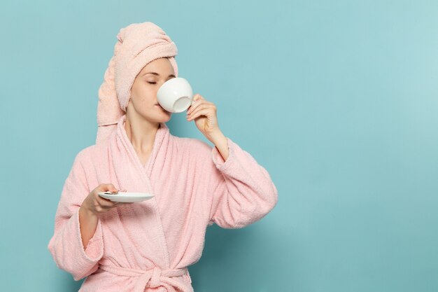 young female in pink bathrobe after shower drinking coffee on blue